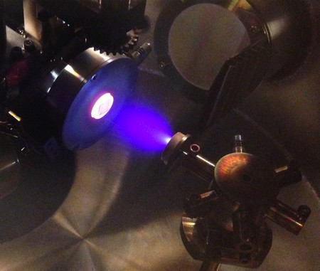 Inside view of vacuum chamber in which the process of 'pulsed laser deposition' takes place, used to create the hafnium oxide crystals in this study. On the left the glowing substrate on which the film is growing with atomic control; in the center the blue plasma of ions that is created by shooting a laser on a target with the right chemical composition (target visible on the right side of the figure). | Photo Henk Bonder, University of Groningen
