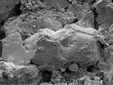 A scanning electron microscopy photograph of a reservoir sandstone sample. Fresh quartz crystals are growing on top of a sand grain, the pore space next to the grain is filled with small crystals of clay minerals and quartz. Width of image ~300 µm. | Photo Miocic lab